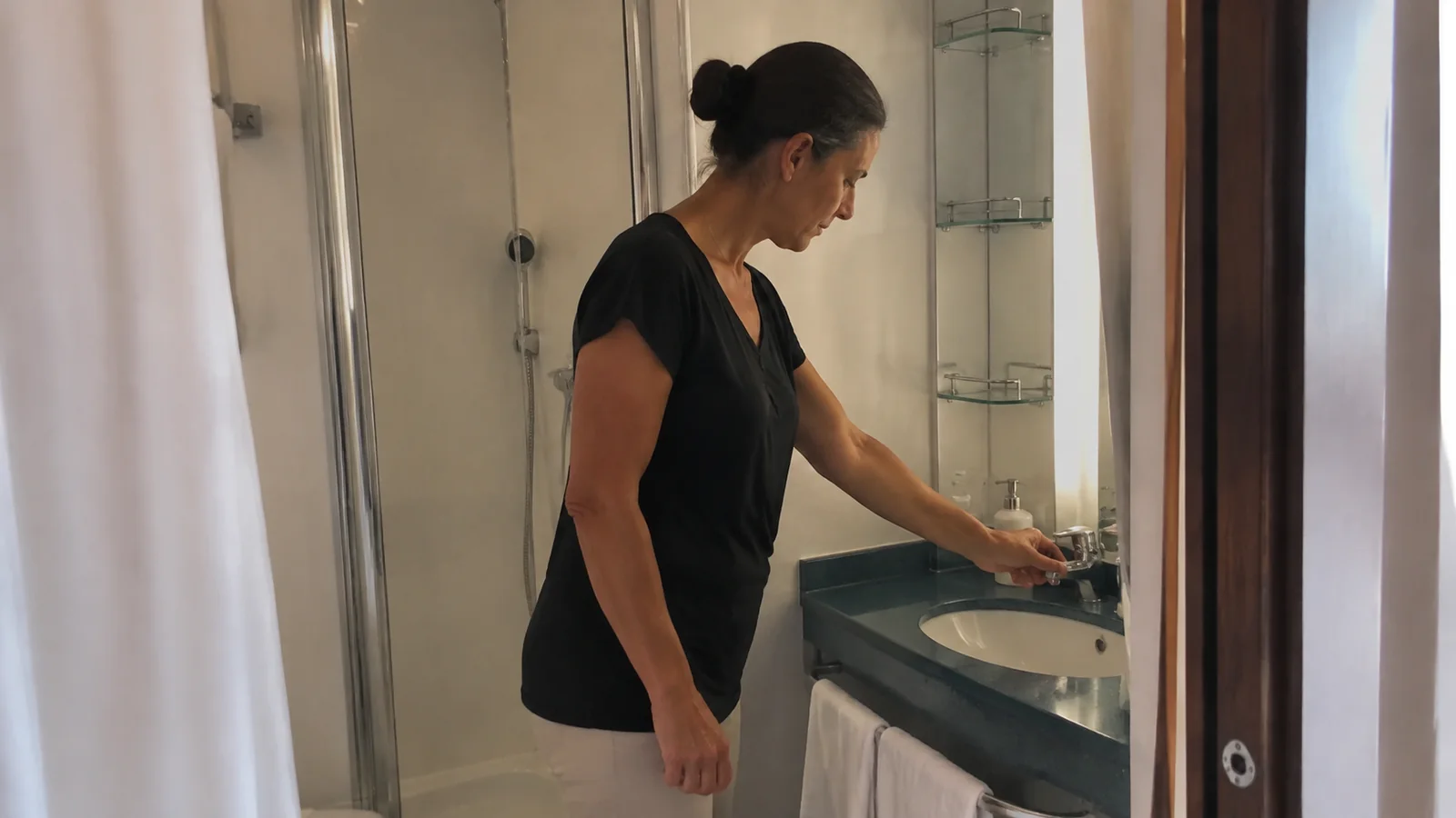 Woman checks the faucet in a compact cabin bathroom.