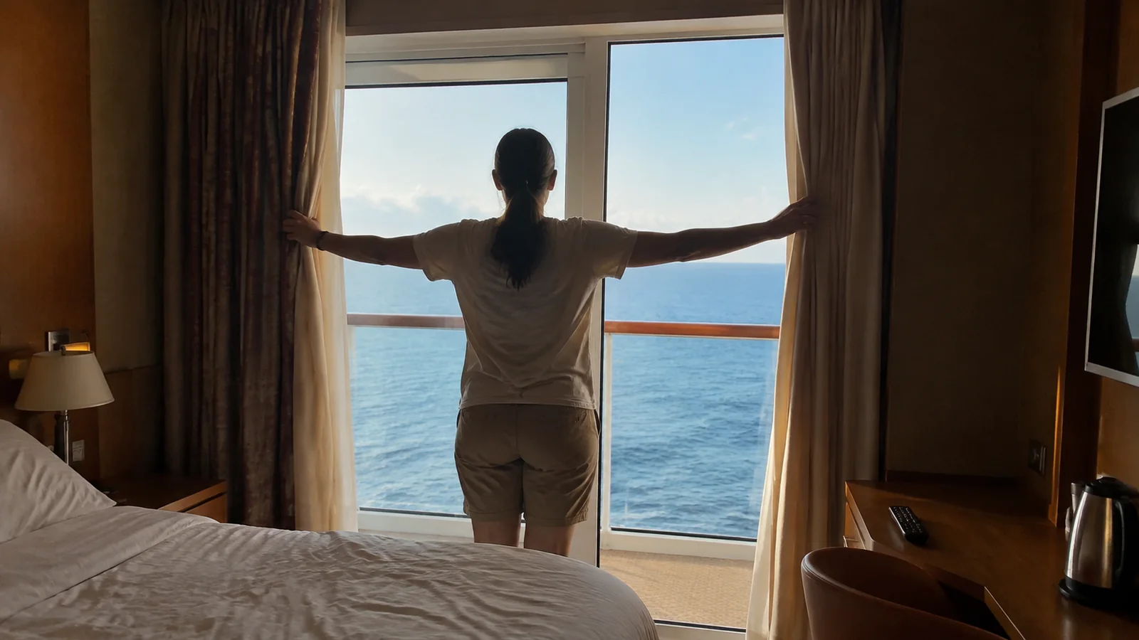 Woman opens cabin curtains to reveal the ocean.