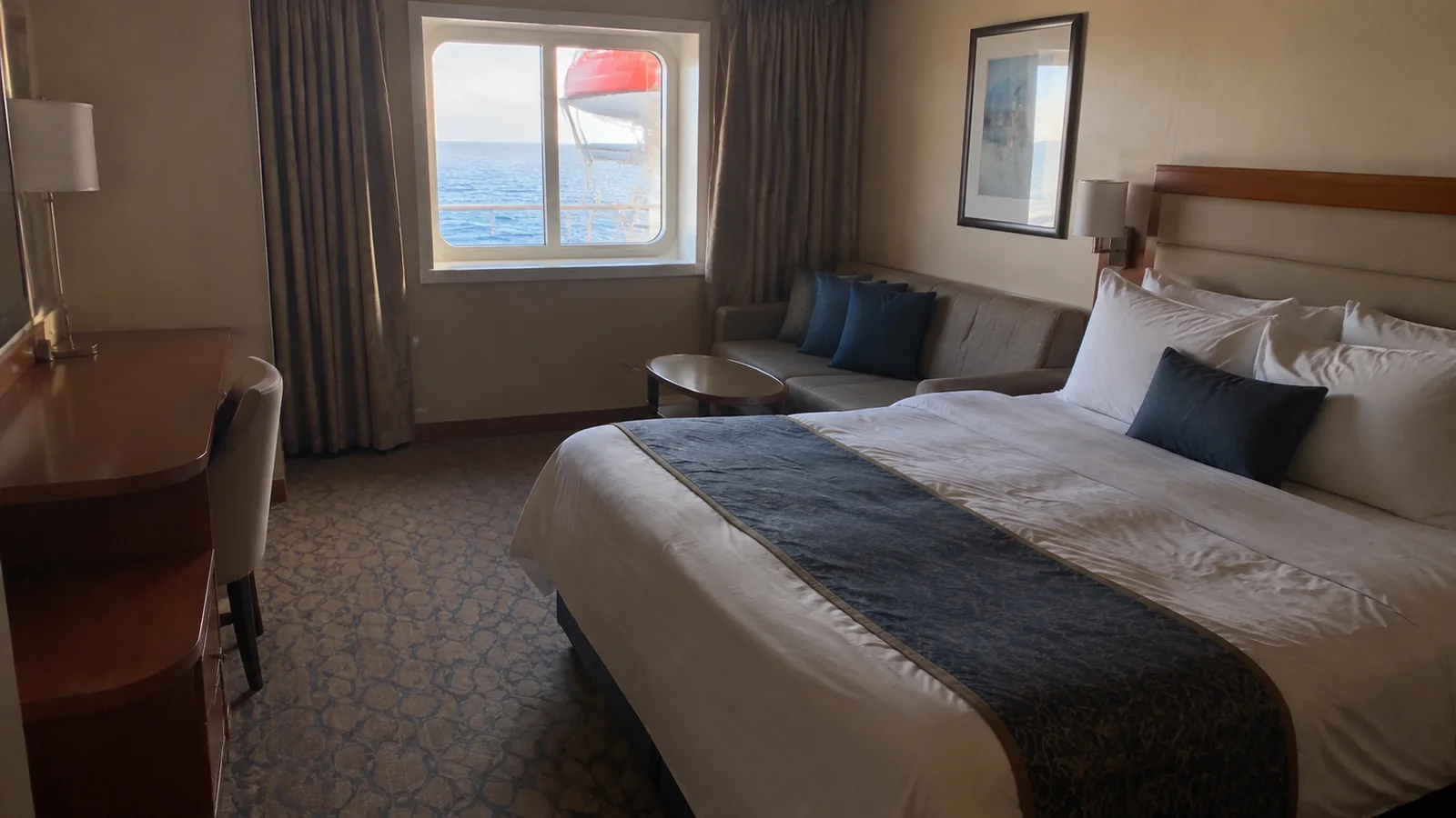 Oceanview stateroom has a double bed, sofa and wooden desk.