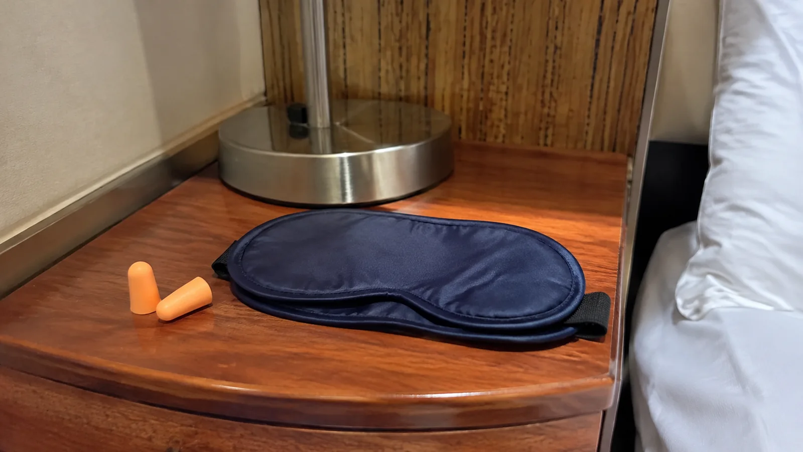 Blue sleep mask and orange earplugs sit beneath a bedside lamp.
