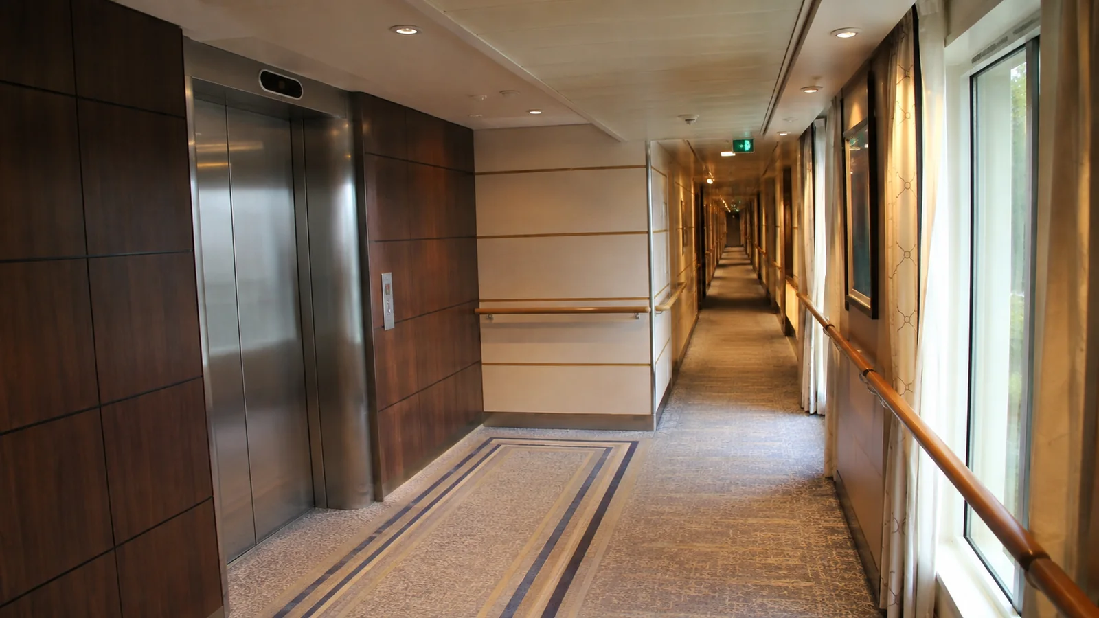 Elevators stand beside a long corridor with wooden handrails.