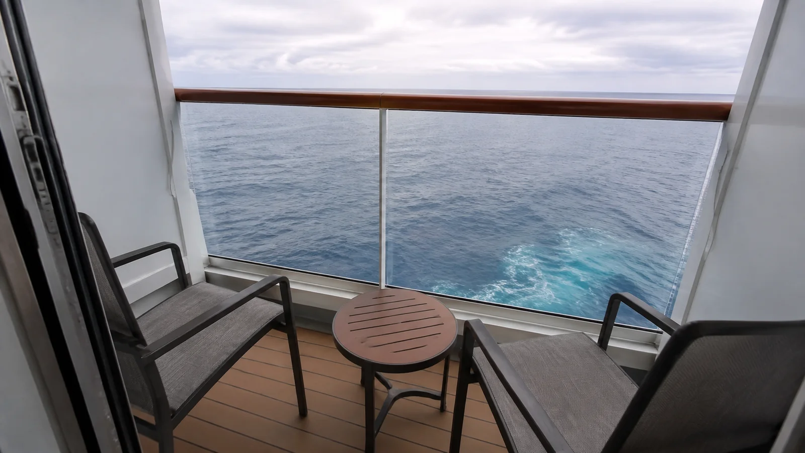 Two chairs and a small table on a balcony overlooking the ship's wake.