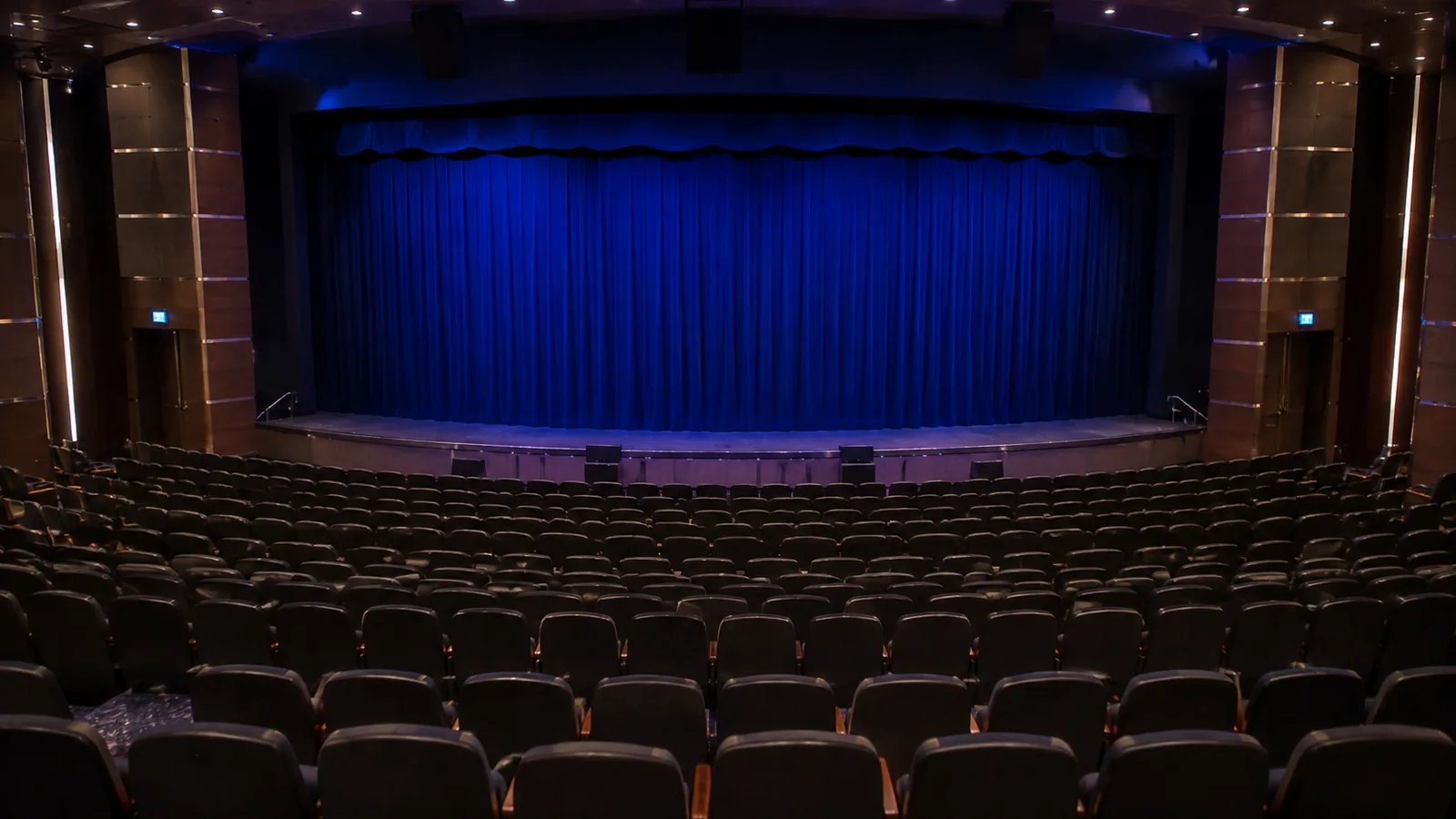 Rows of empty theater seats face a closed blue curtain.