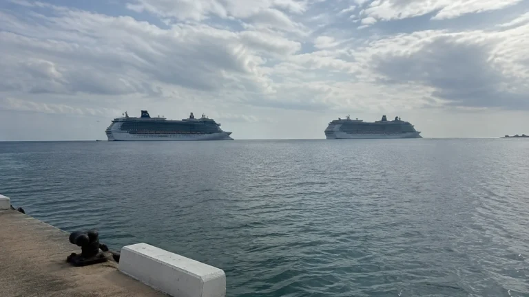 Two large cruise ships sit offshore beneath a cloudy sky.