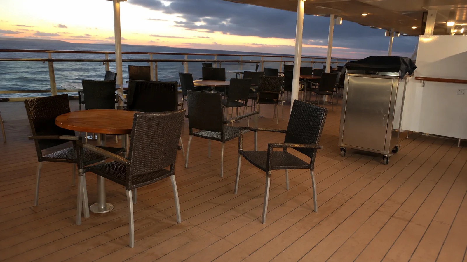 Empty tables and chairs on an outdoor ship deck at sunset.
