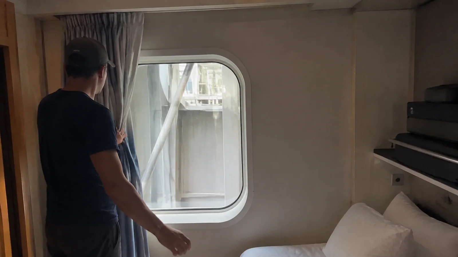 Man facing a cruise cabin window obstructed by exterior ship equipment