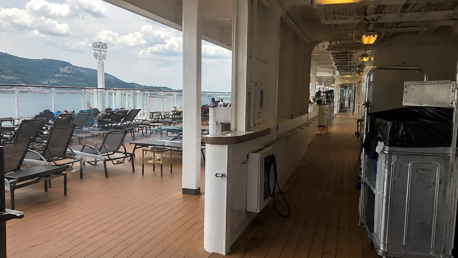 Cruise ship promenade with lounge chairs and a covered walkway in port