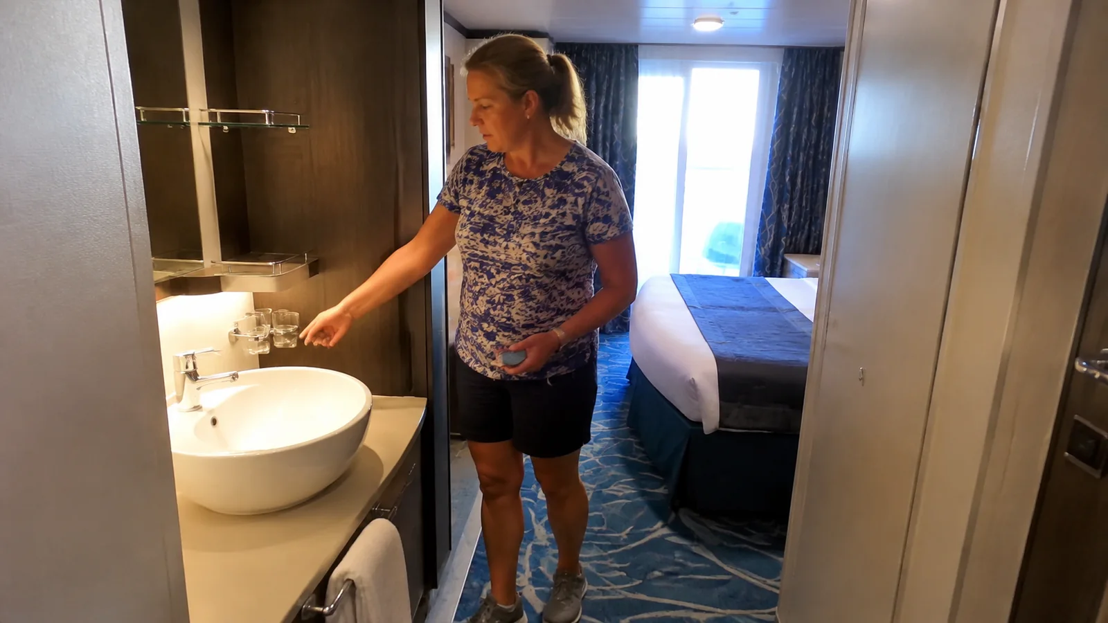 Woman stands beside a basin near a stateroom entrance.
