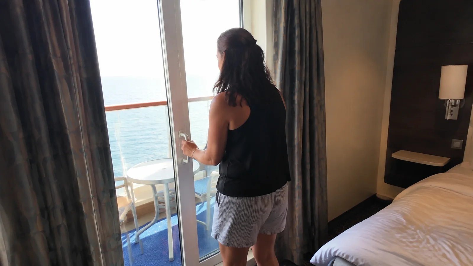 Woman stands at an open cabin balcony door overlooking the sea.