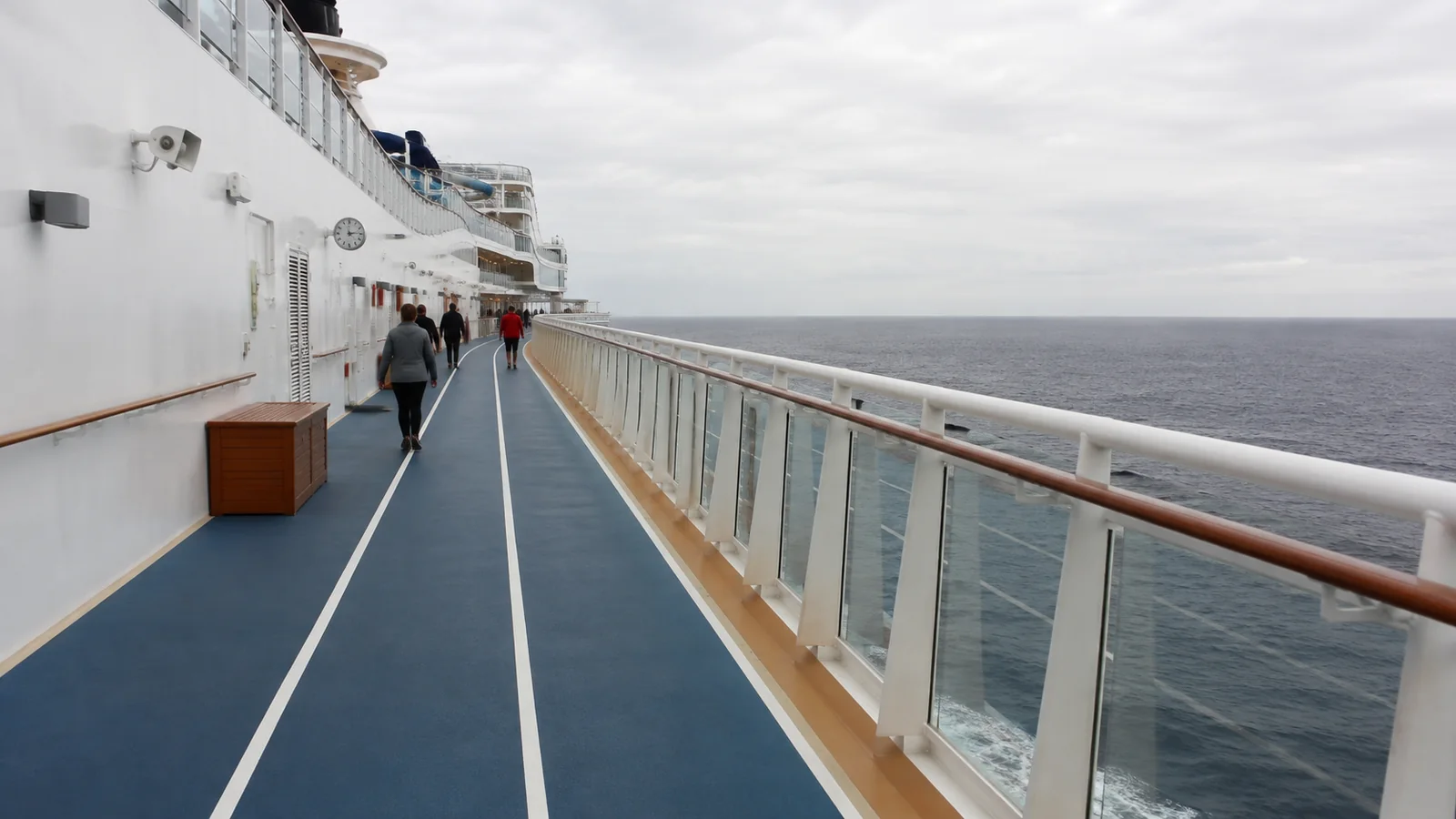 Passengers walk along a blue outdoor track beside the ocean.