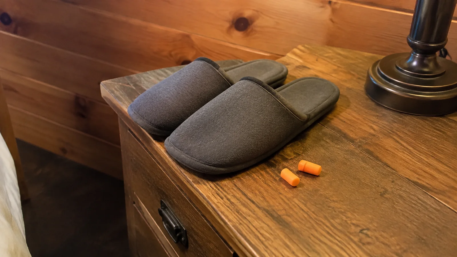 Gray slippers and orange earplugs on a wooden bedside table.