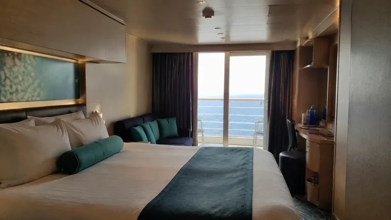 Balcony cabin with teal cushions, a double bed and small sofa.
