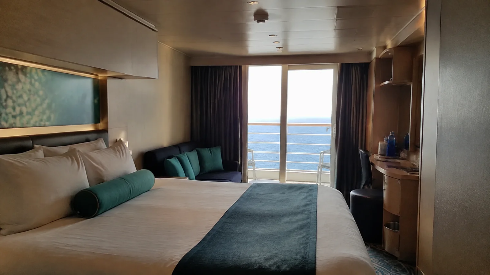 Balcony cabin with teal cushions, a double bed and small sofa.