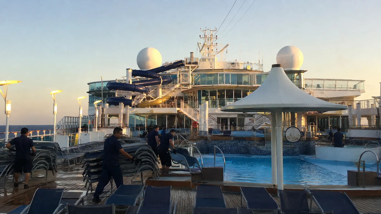 Crew arranging loungers around an outdoor ship pool.