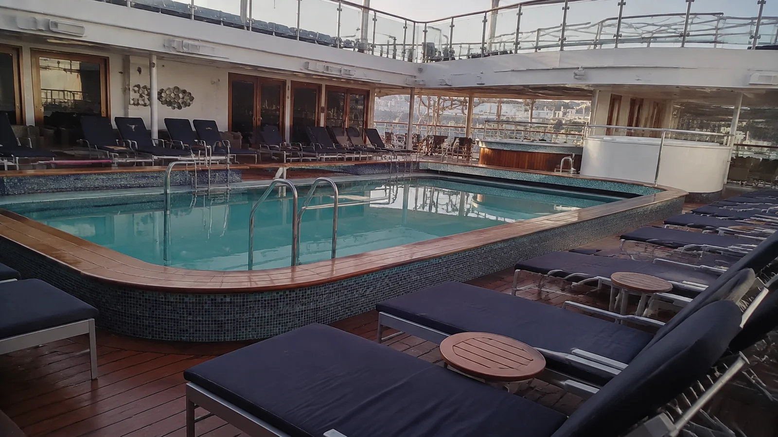 Empty loungers surround a rectangular pool on a ship deck.