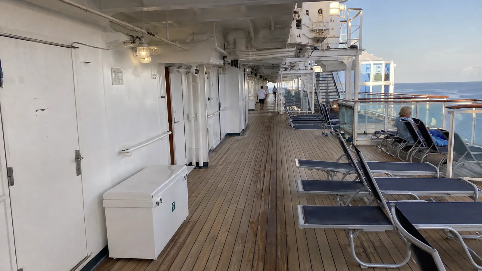 Lounge chairs along a wooden cruise ship promenade overlooking the ocean