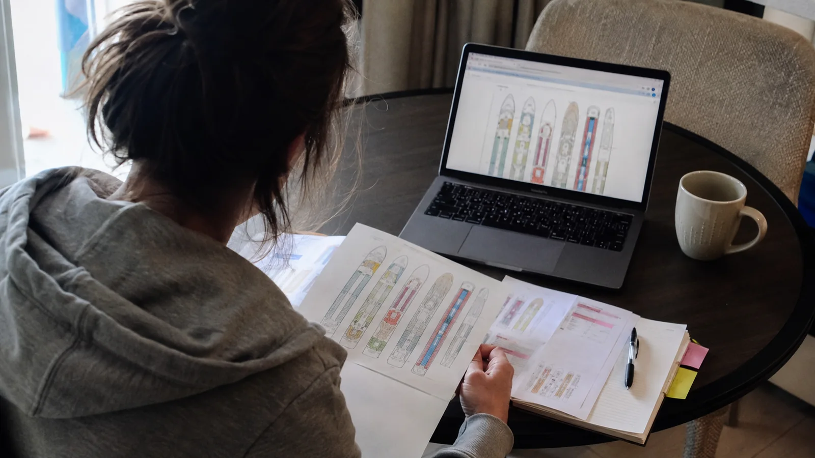 Woman reviewing printed cruise ship deck plans beside a laptop