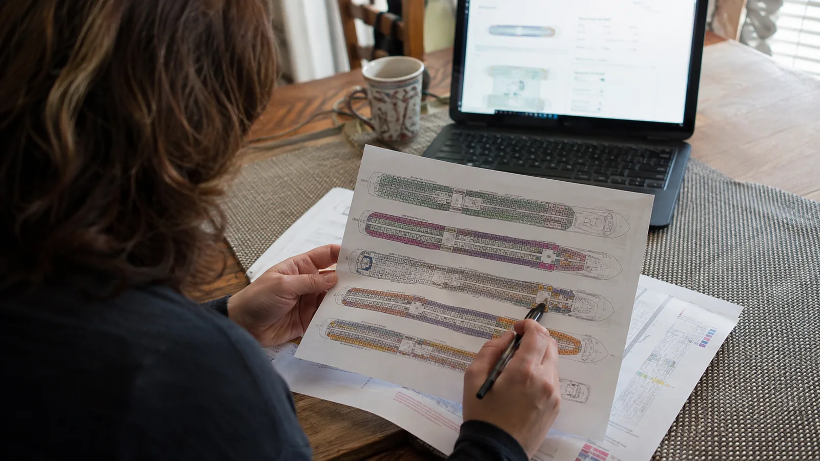 Woman marking a printed cruise ship deck plan beside a laptop