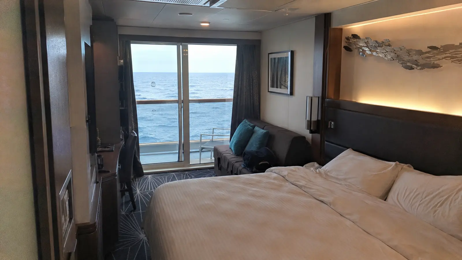 Cruise cabin with a bed, sofa, and balcony overlooking the ocean