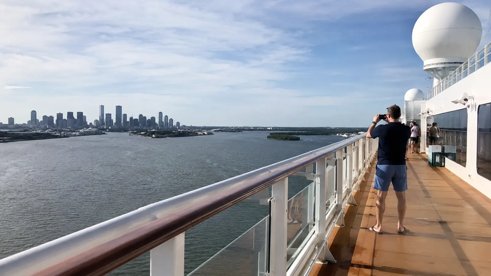 Cruise ship outer deck overlooking a coastal city skyline with a man taking a photo
