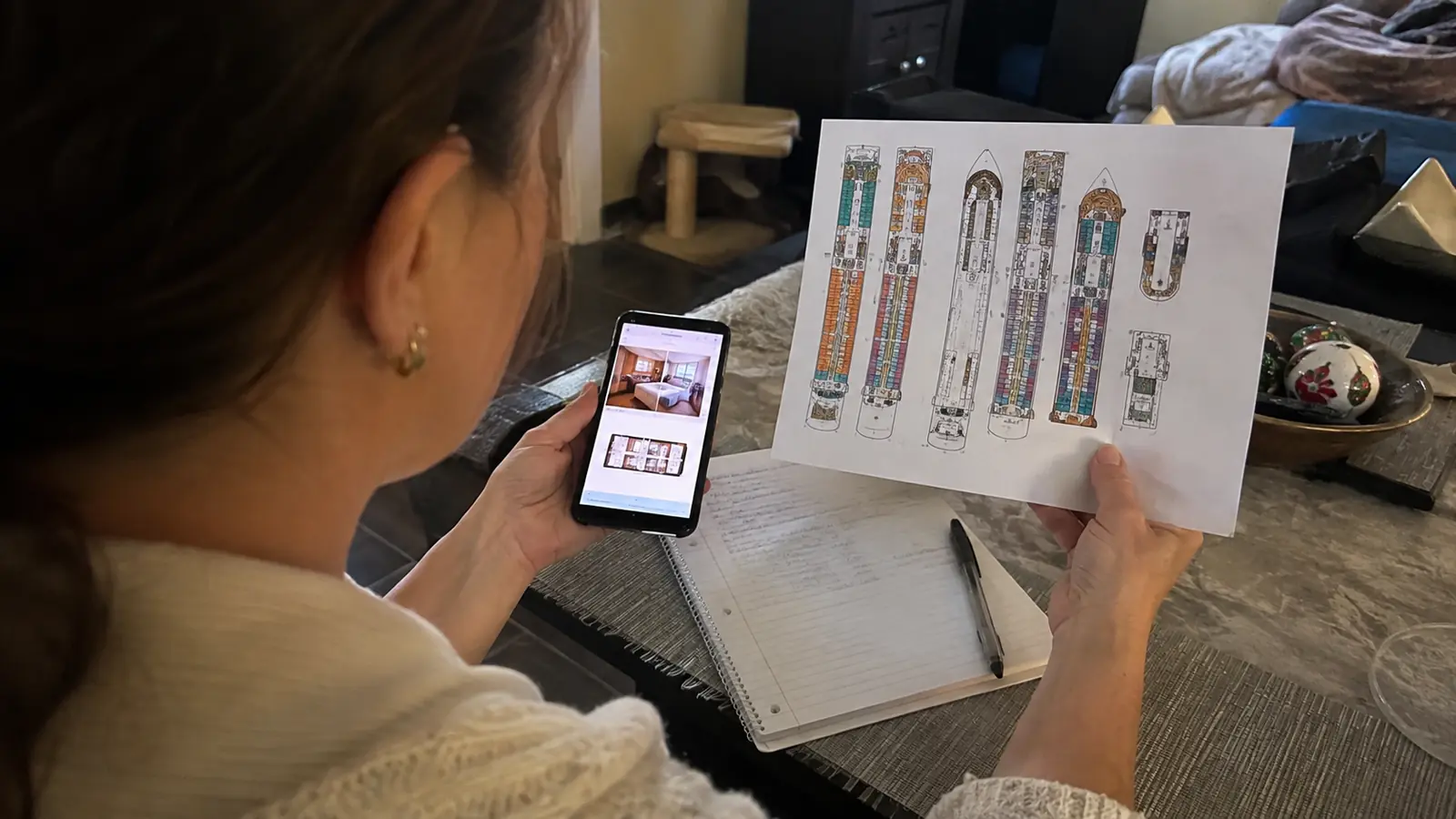 Woman holding a printed cruise ship deck plan and smartphone in a cabin