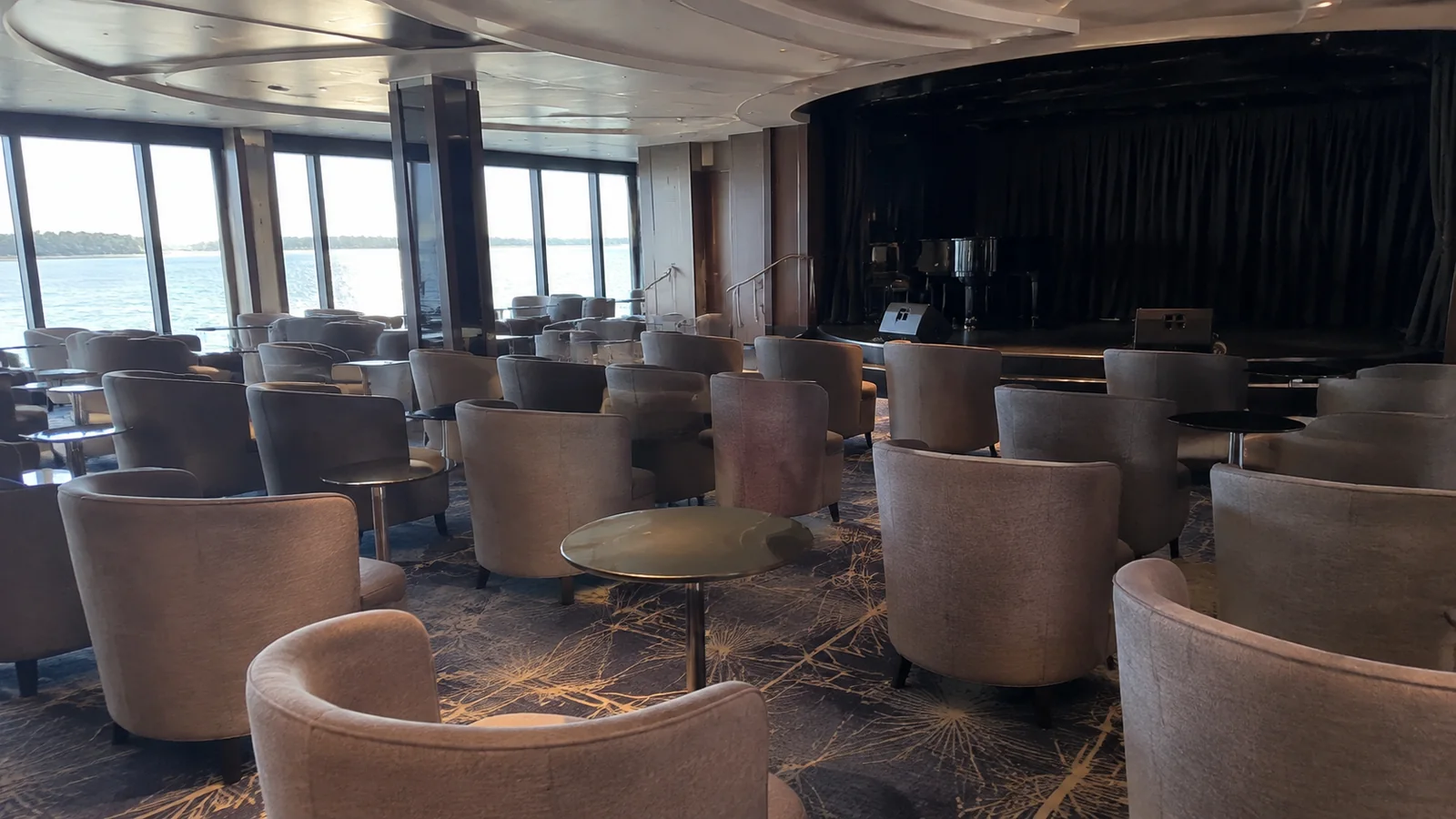 Empty lounge chairs face a curtained stage beside tall windows.