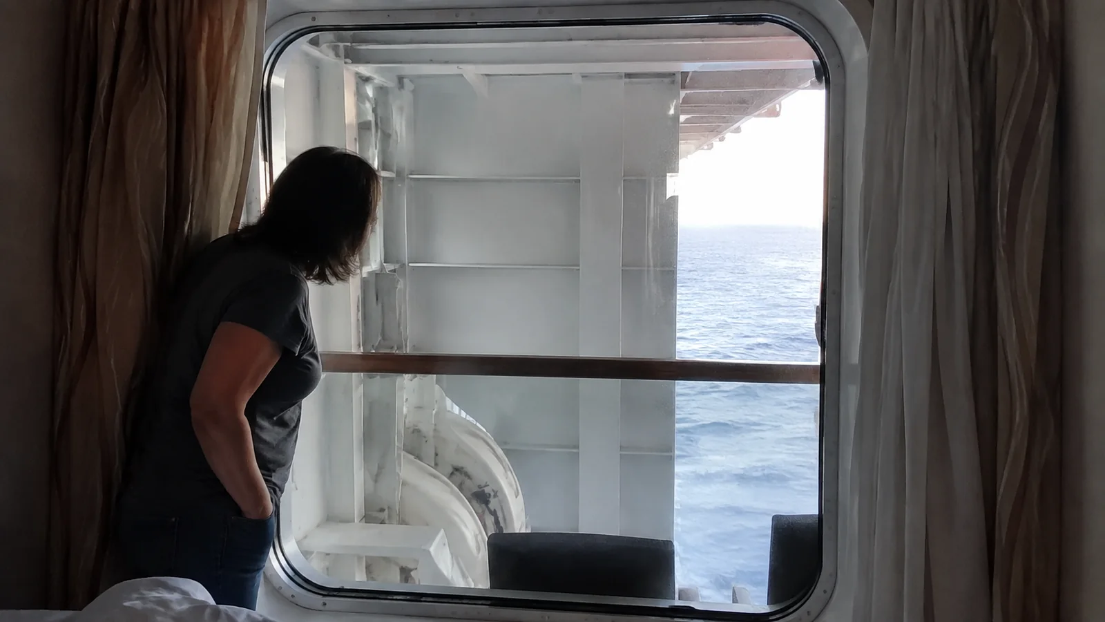 Woman looking through a cruise cabin window partly blocked by an exterior structure