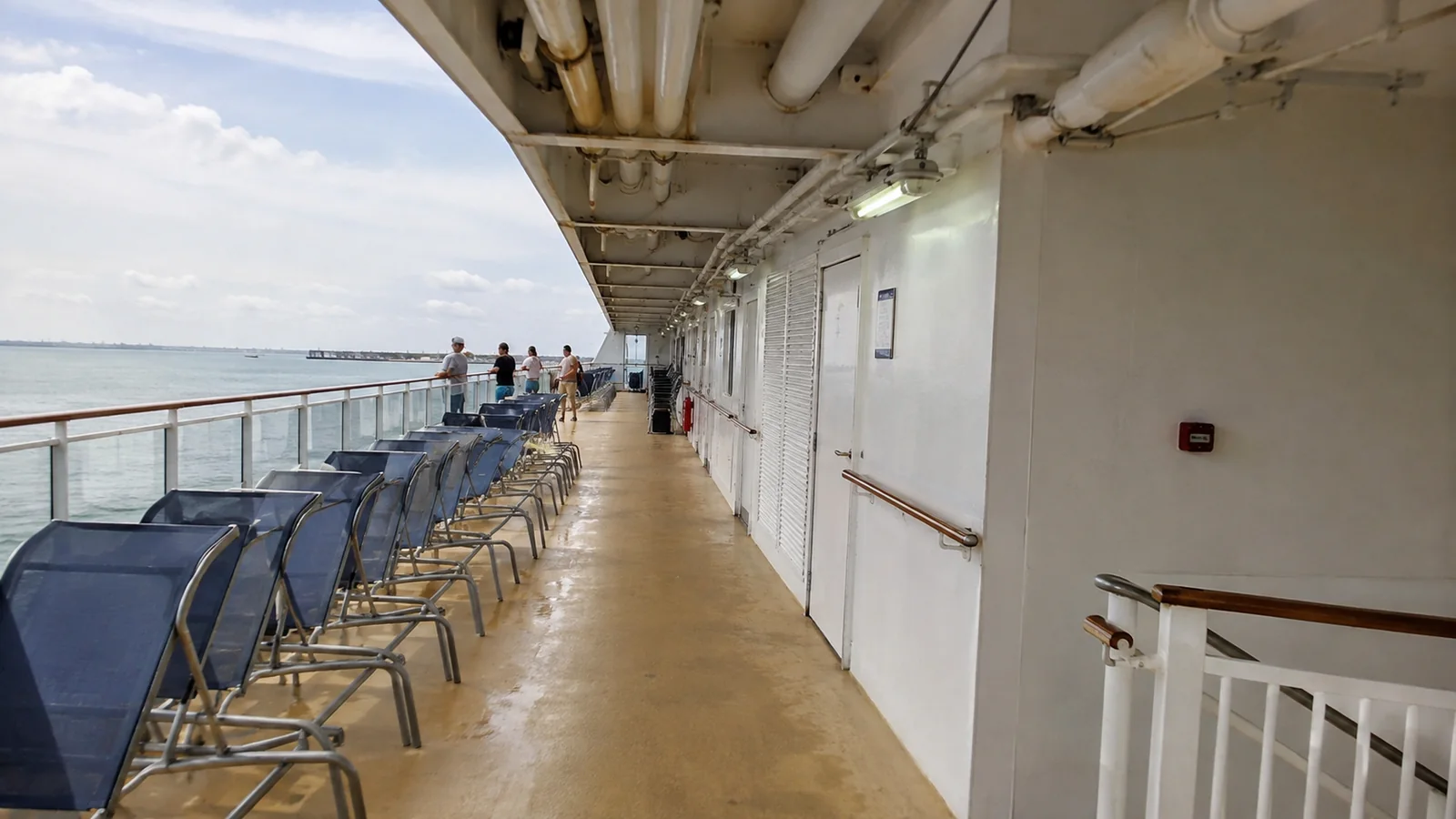 Empty lounge chairs along a covered cruise ship promenade