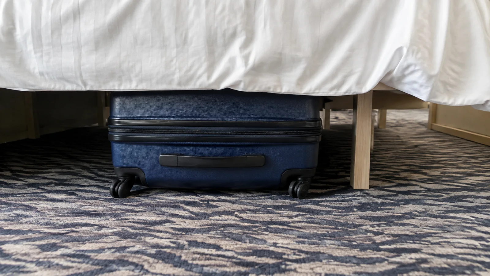 Blue wheeled suitcase is stored beneath a stateroom bed.