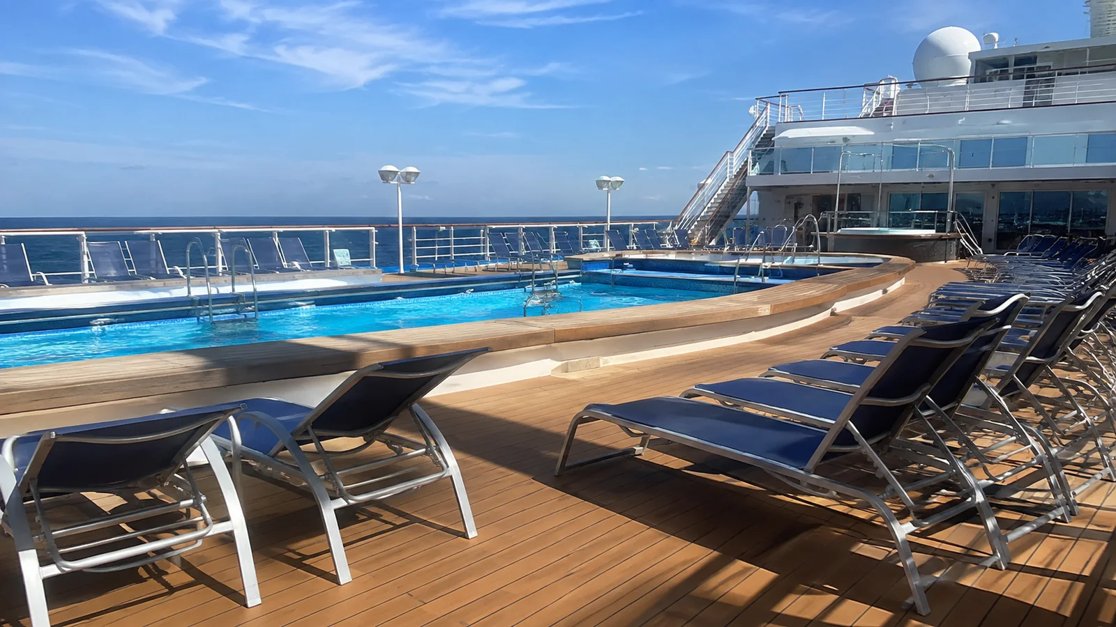Empty blue loungers surround an outdoor cruise ship pool.