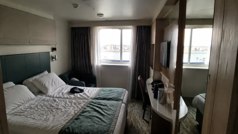 Cruise cabin with a double bed, mirrored wardrobe, and window