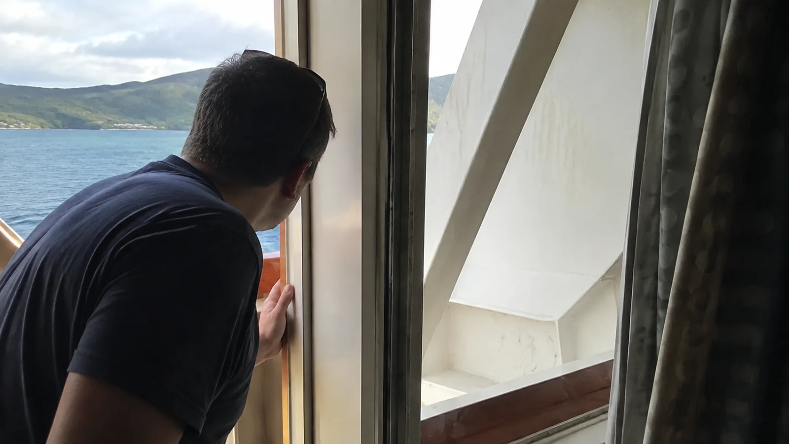 Man looking past a diagonal support from a cruise cabin balcony doorway