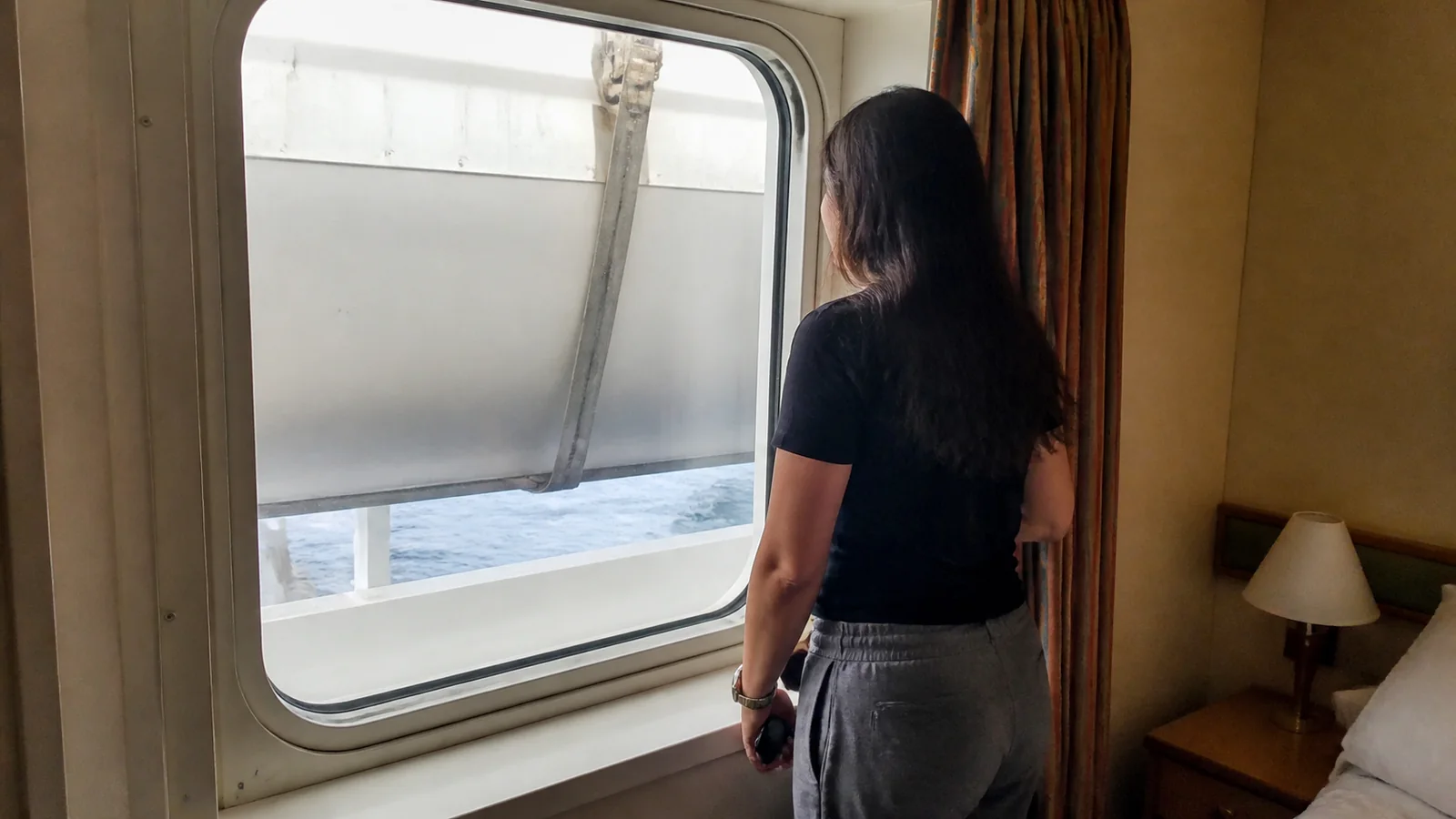 Woman facing a cruise cabin window partly blocked by an exterior panel