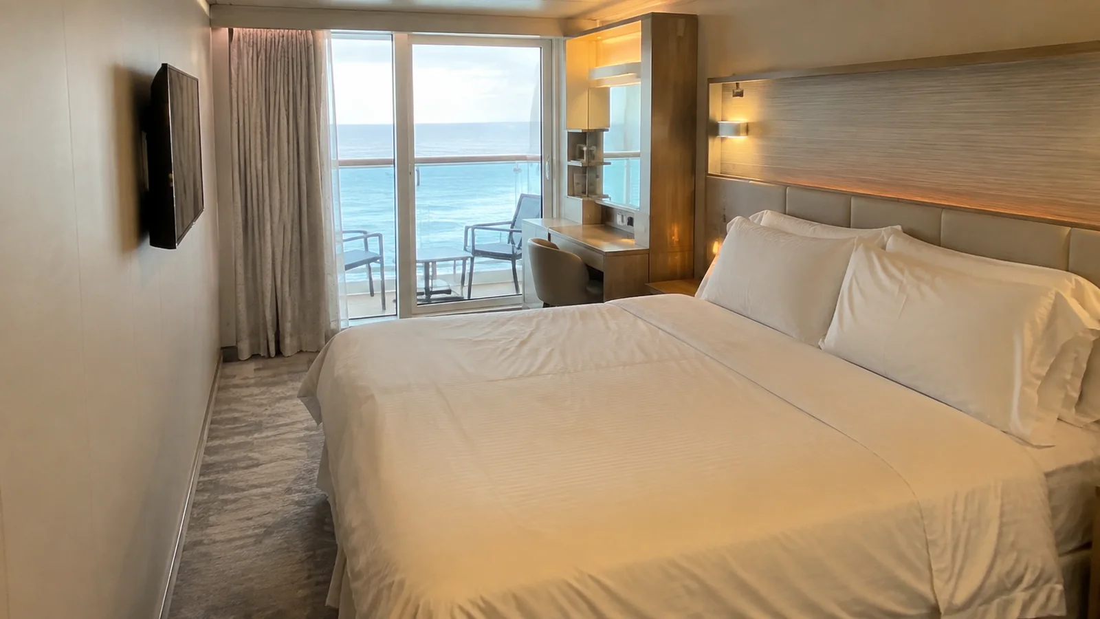 Modern stateroom contains a large bed and ocean balcony doors.