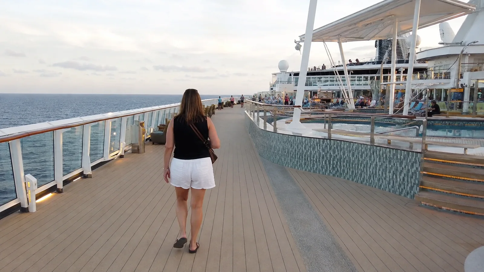 Woman walks along an open ship deck beside a pool.