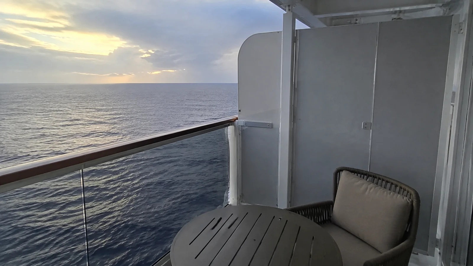 Balcony chair sits beside a tall partition overlooking the sunset.