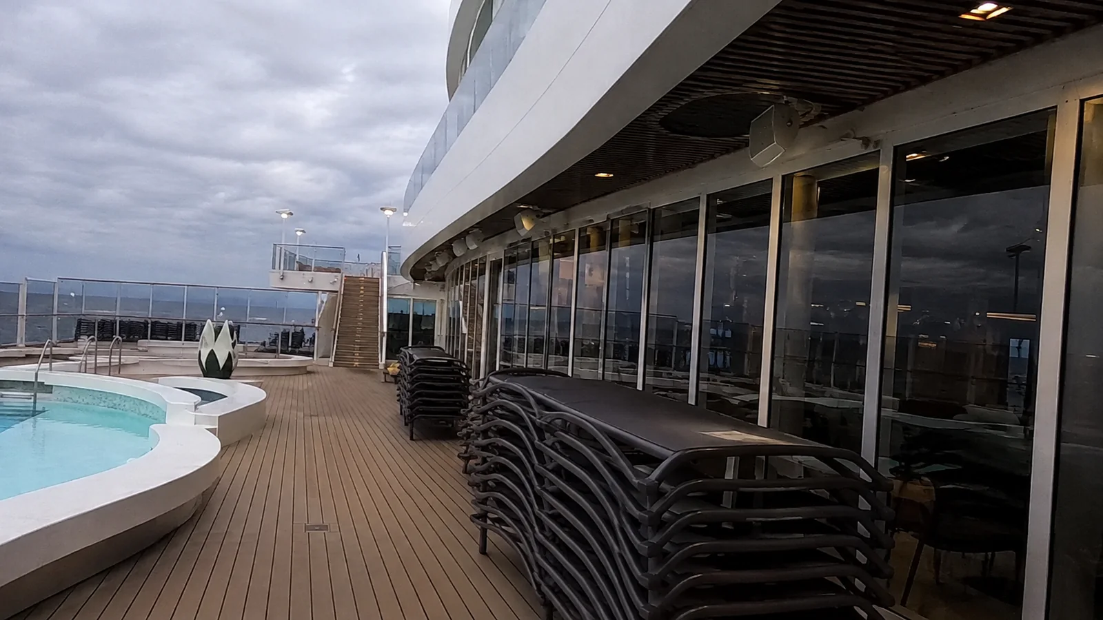 Stacked loungers line restaurant windows beside an empty ship pool.