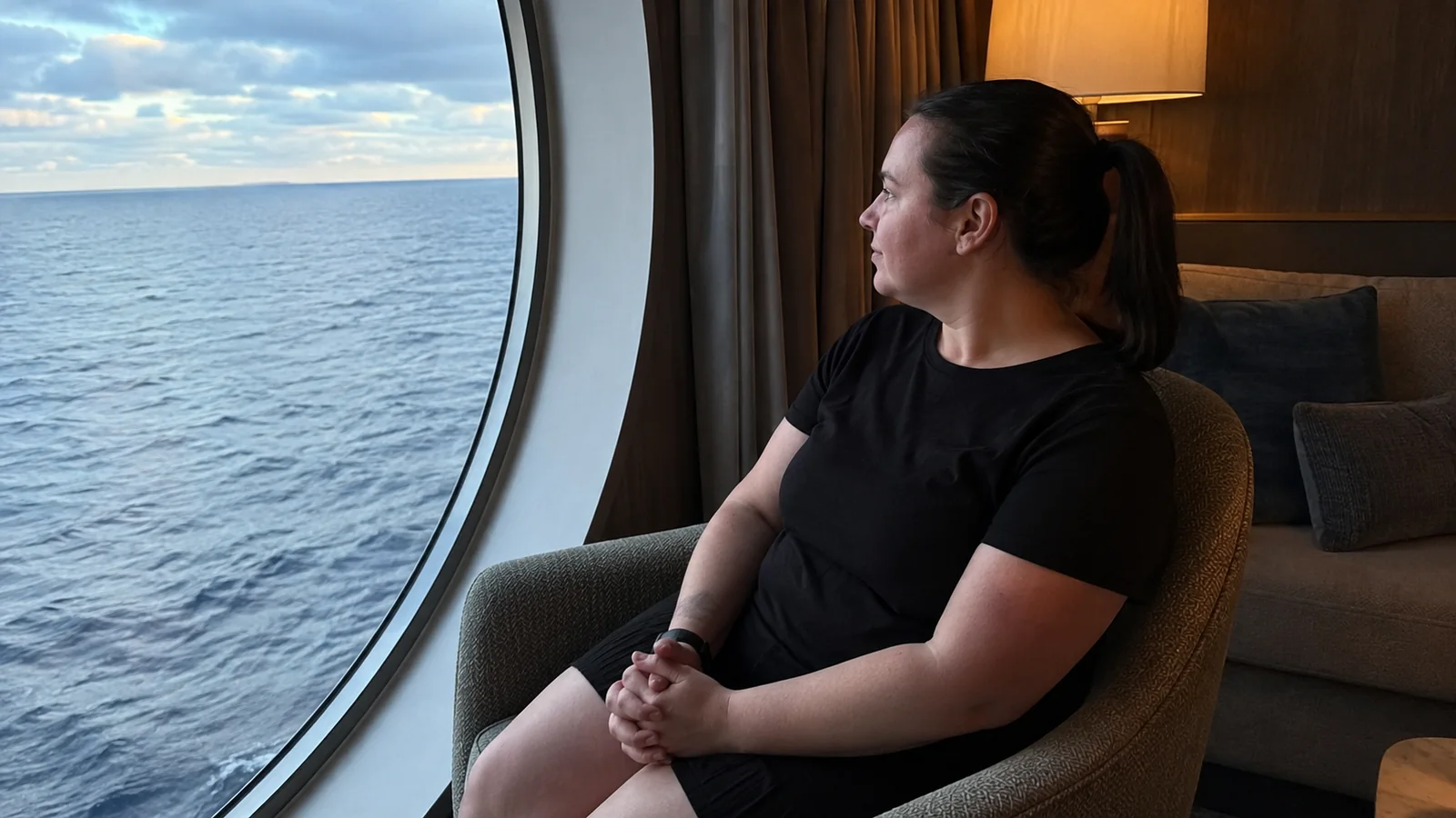 Woman sits in a chair beside a large ocean window.