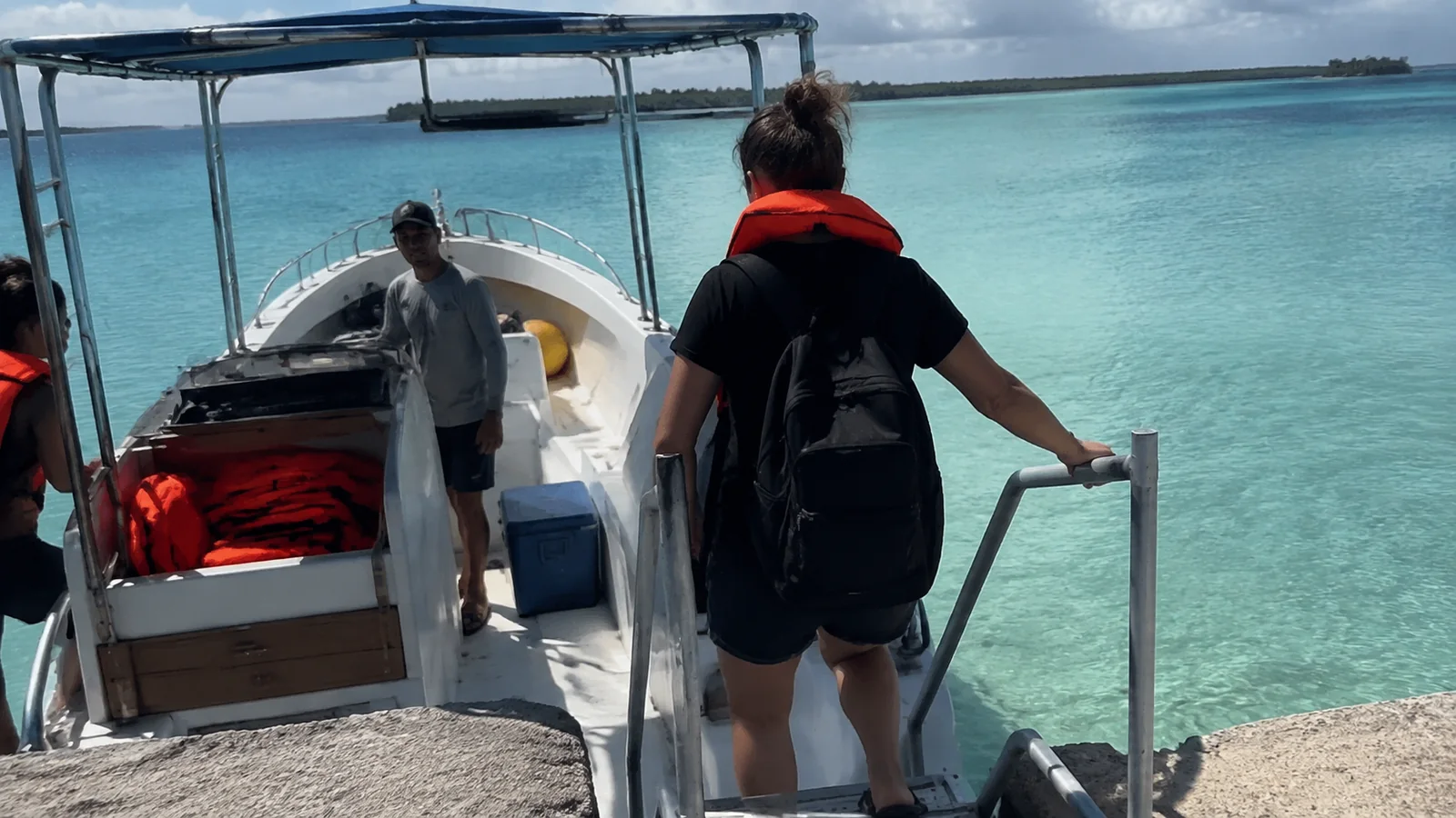 Passengers boarding a small boat beside bright turquoise water.