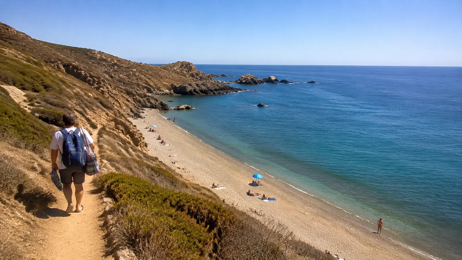 Two people walking down a coastal trail toward a secluded beach