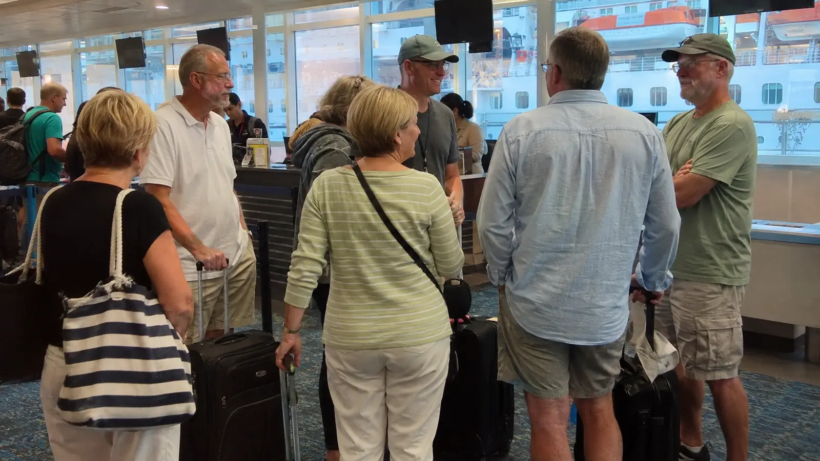 Travelers with rolling luggage waiting inside a cruise terminal