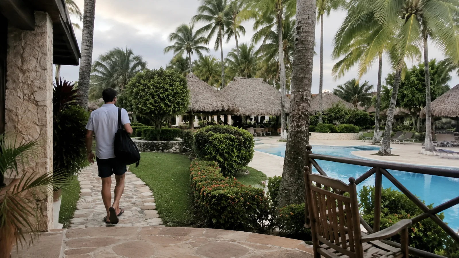 Man walking through palm-lined resort grounds beside a pool