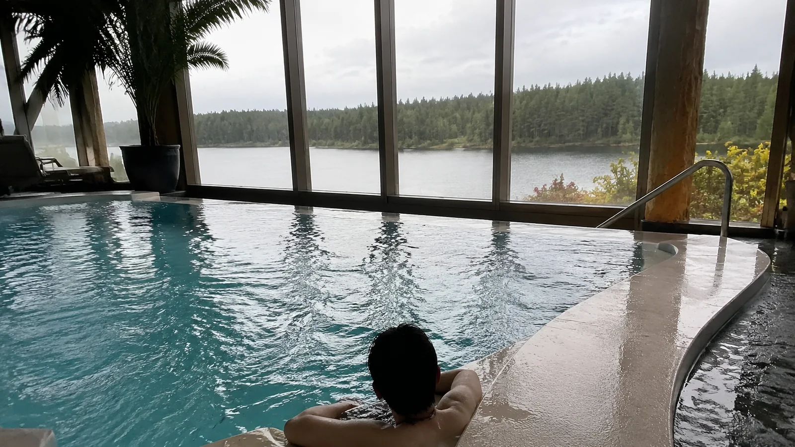 Person relaxing in an indoor pool beside floor-to-ceiling windows