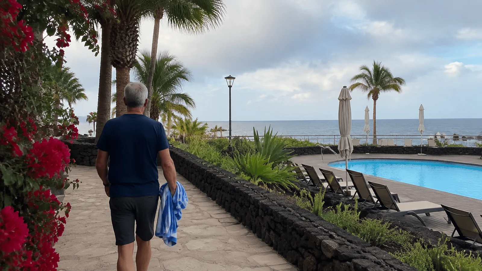 Man walking beside a resort pool carrying a towel