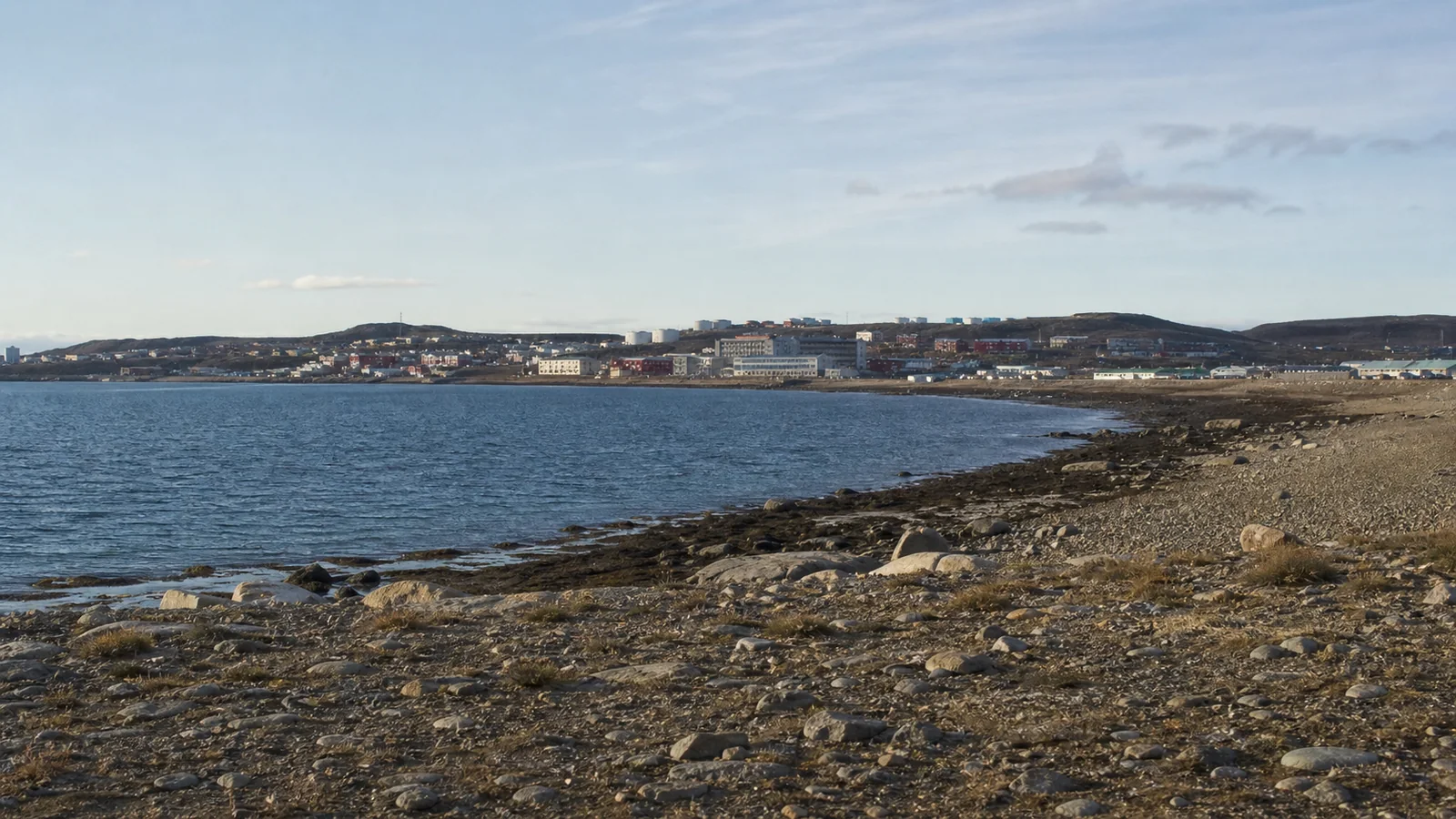 Low coastal settlement across a rocky bay beneath pale skies.