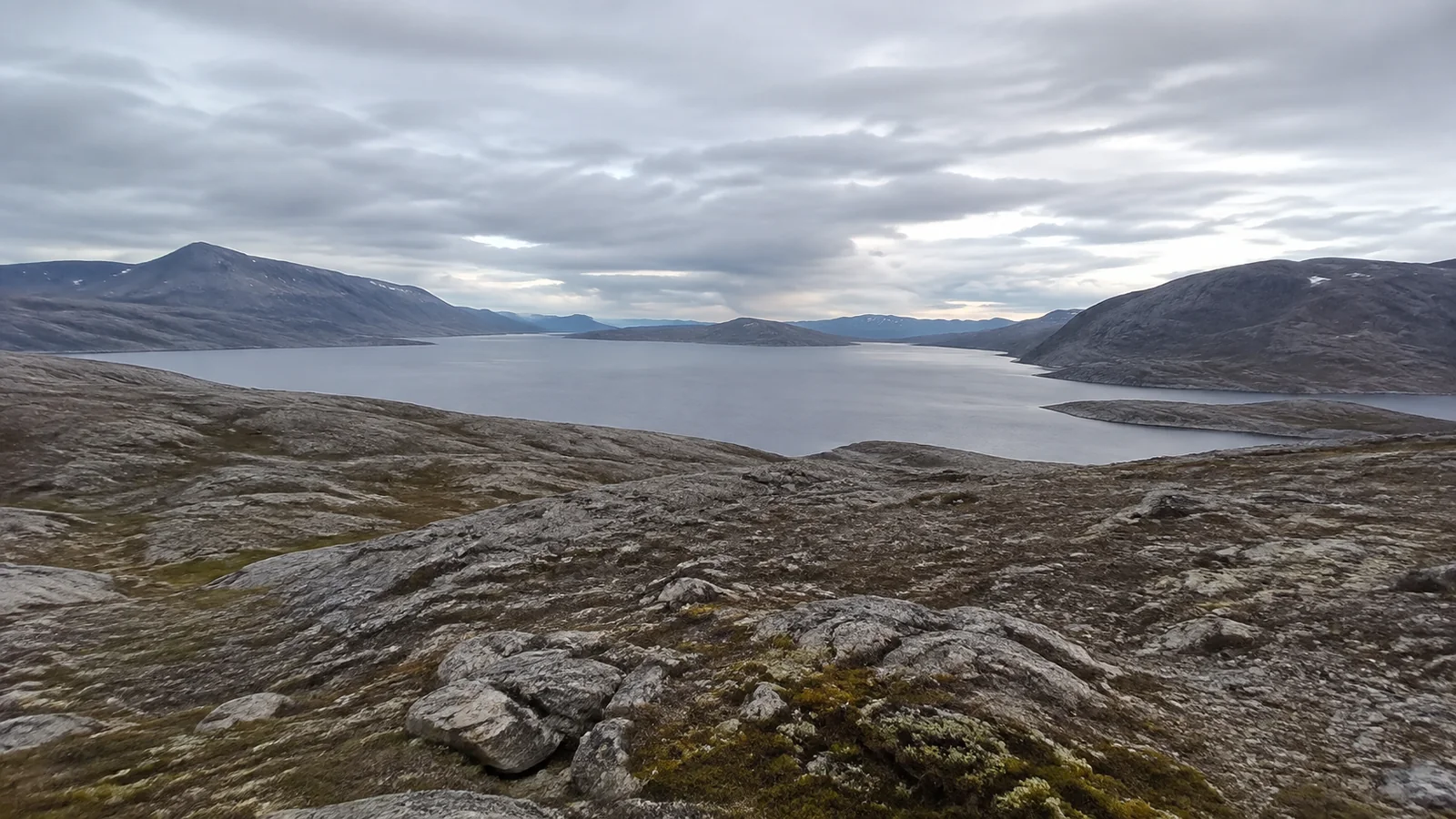 Barren rocky hills surround a wide inlet beneath layered clouds.