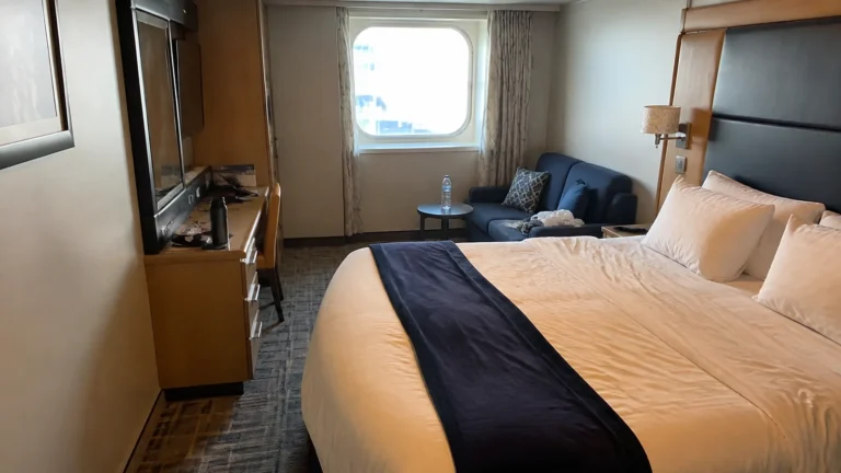 Cruise cabin with a double bed, blue sofa, and window