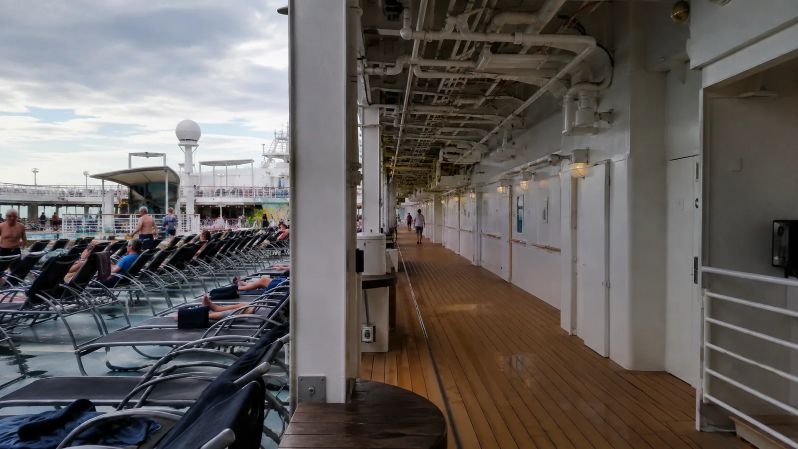 Covered cruise ship walkway beside rows of occupied lounge chairs