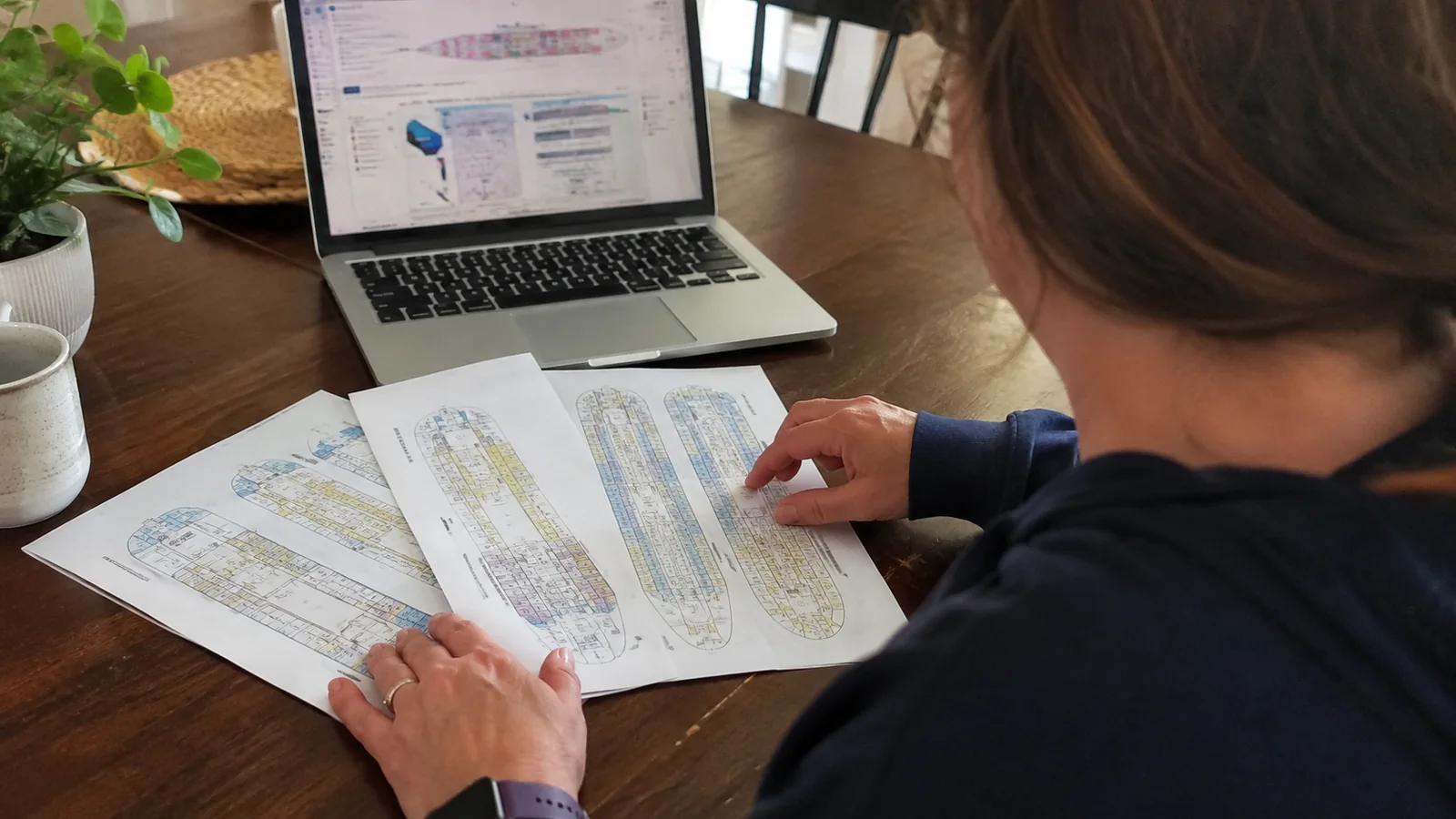 Woman reviewing printed cruise ship deck plans at a table with a laptop