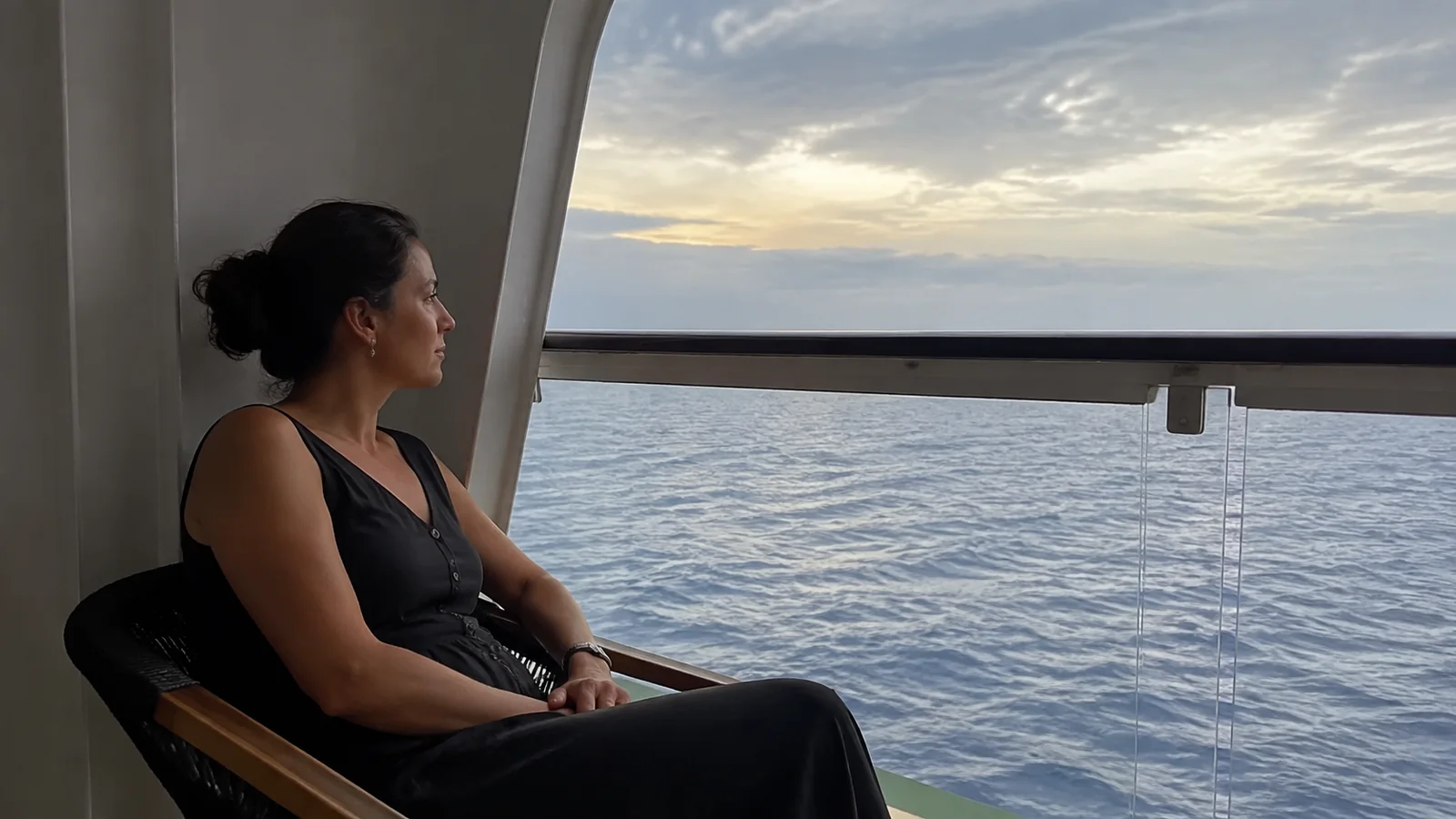 Woman sits on a sheltered balcony facing the ocean.